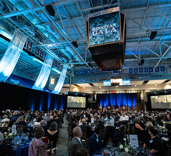 Мужчина в церемониальной одежде поднимает диплом с надписью «Gonzaga University»